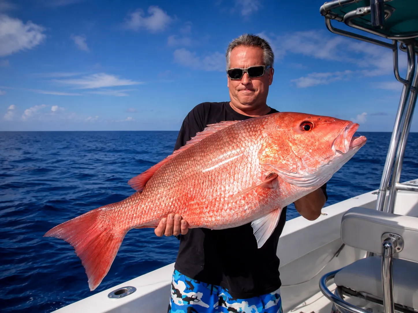 Angler holding a large red snapper on the deck of a fishing boat